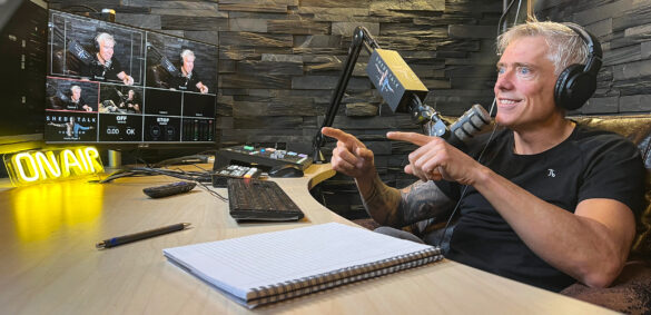 Man with headphones points while recording podcast in studio with 'On Air' sign.