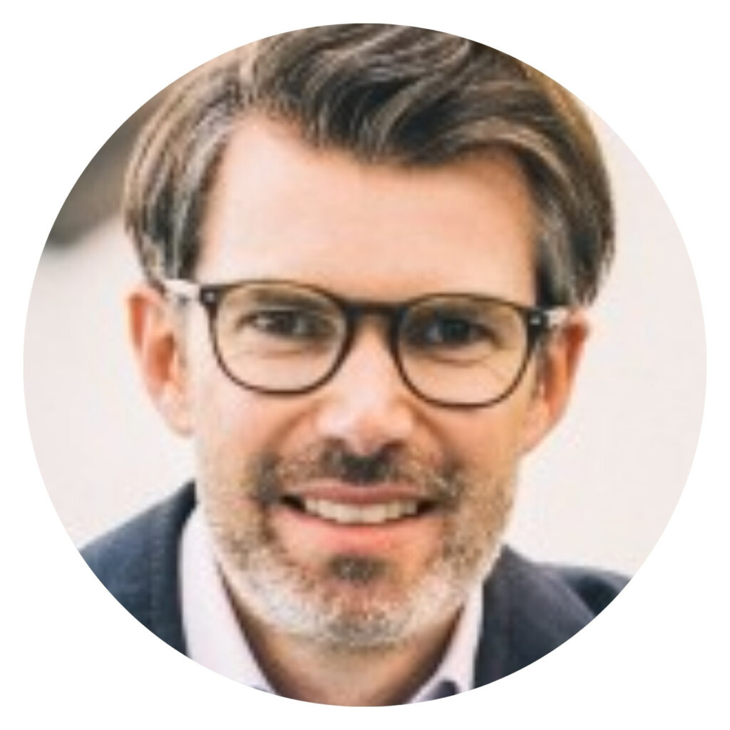 Man with glasses and beard smiles for a profile picture
