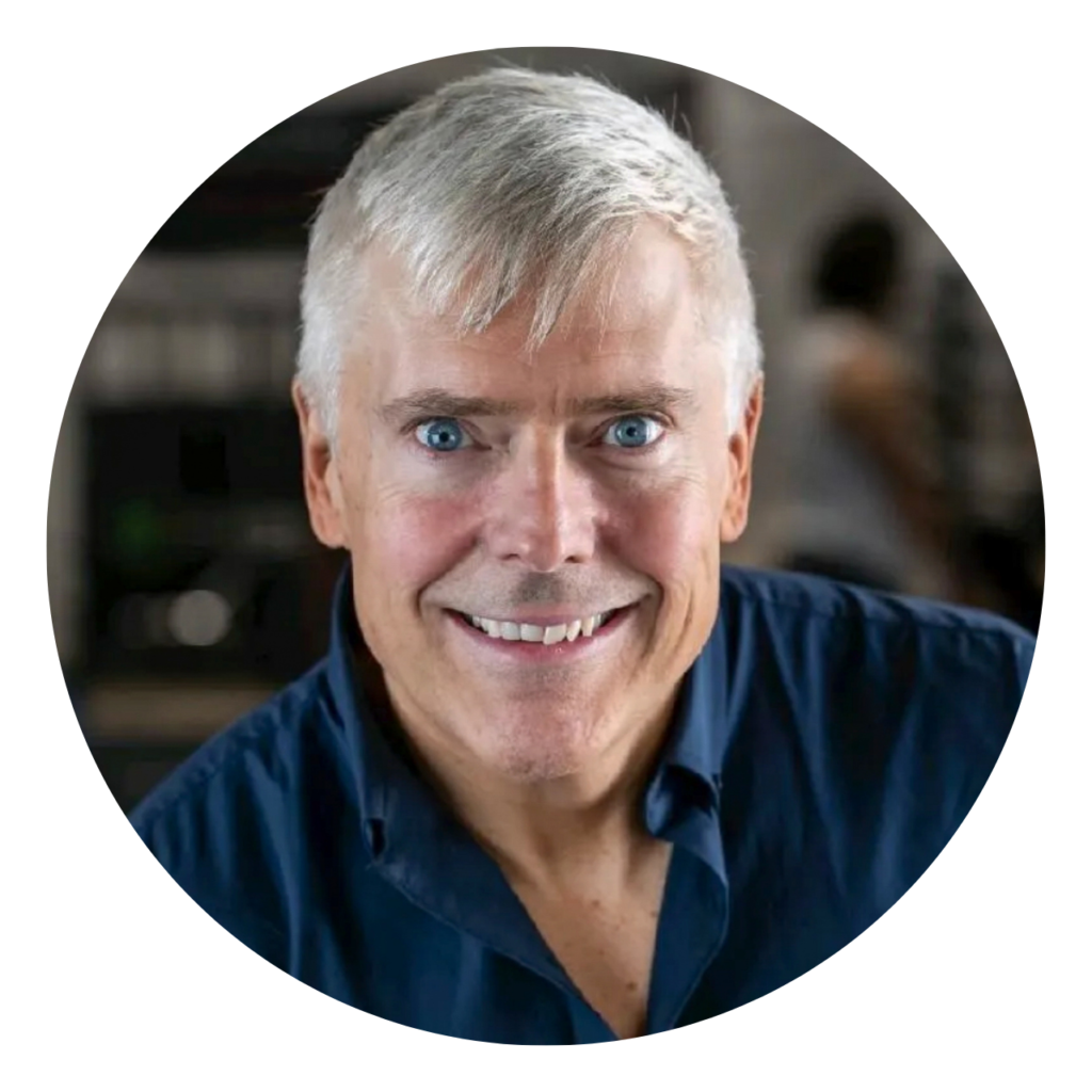 Man with grey hair and blue eyes smiling in a dark blue shirt