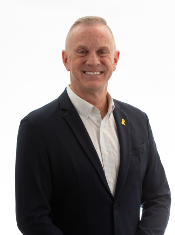 Man in a navy suit with a yellow ribbon pinned to lapel smiling against white background