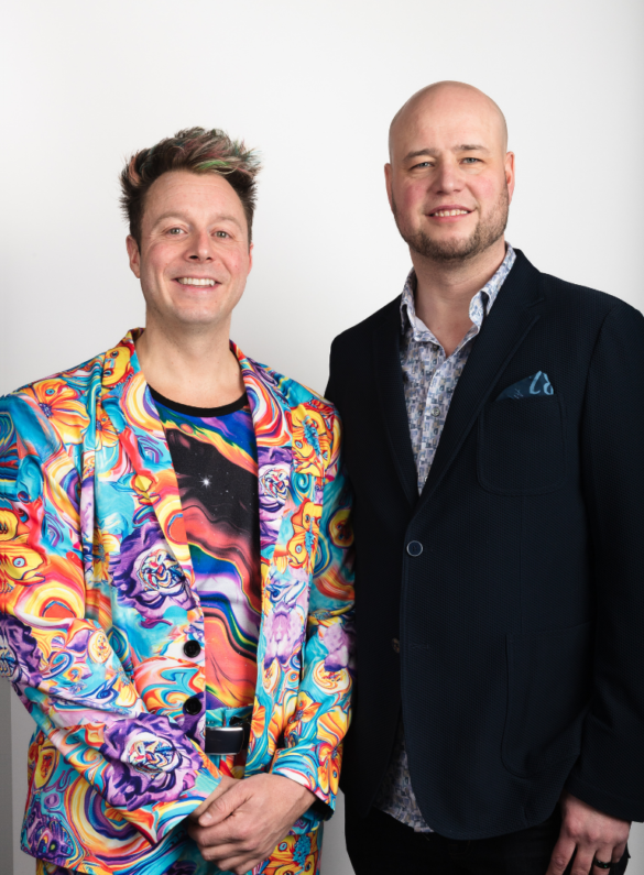 Two men posing. One wears a colourful patterned suit, the other a dark blazer.