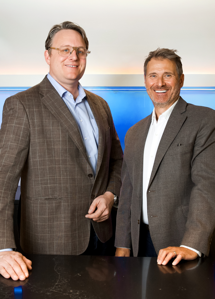 Two men in suits smiling beside each other at a counter