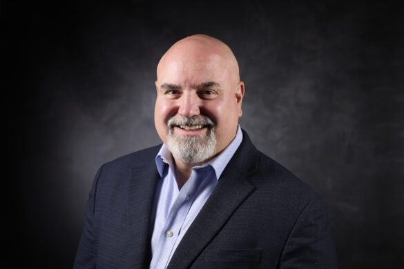 Bald man with a goatee smiling in a dark blazer and light blue shirt