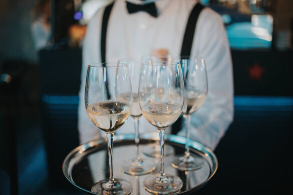 Waitperson in formal attire serving white wine in glasses on a silver tray