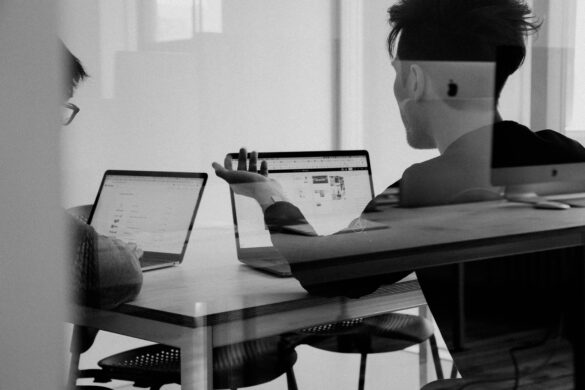 Two people collaborate on laptops at a modern office desk.