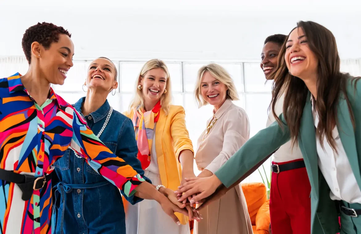 Diverse women in colourful attire laughing and joining hands in a circle.