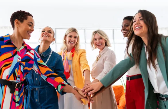 Diverse women in colourful attire laughing and joining hands in a circle.