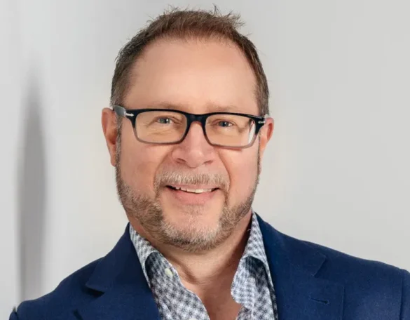 Man with beard and glasses wearing a blue blazer and checkered shirt smiling