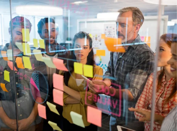 Diverse team collaborates on a glass wall with sticky notes and diagrams.