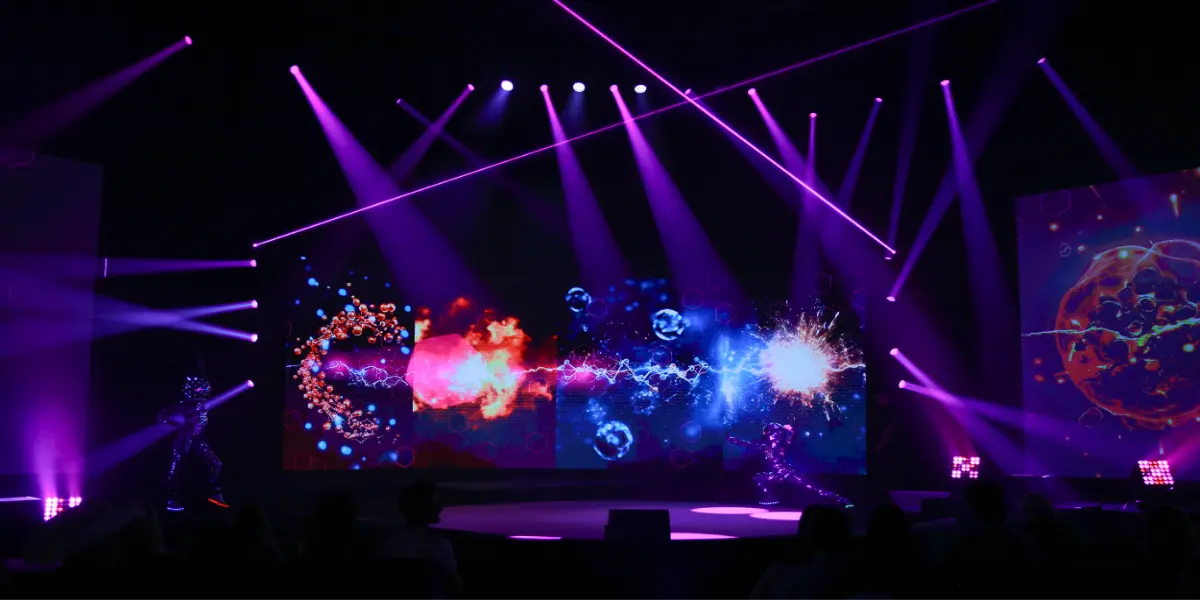 Robots in LED suits perform on stage with purple lights and visual screens.