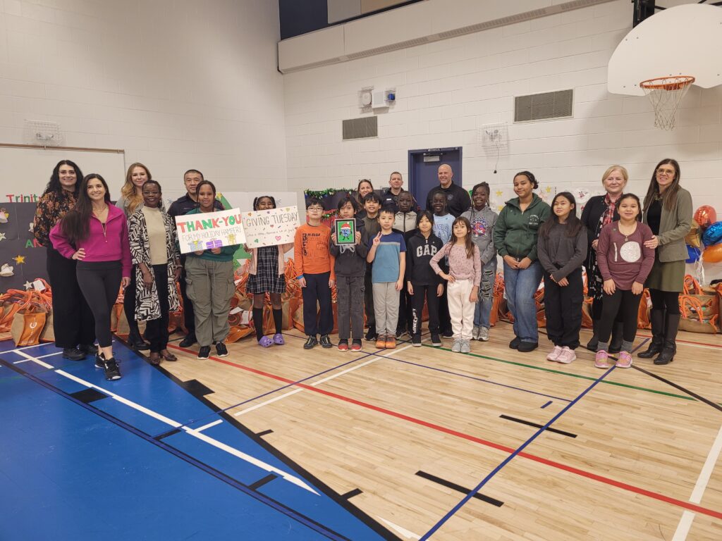 Volunteers and children pose with a "Thank You Giving Tuesday" sign in a gymnasium.