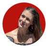 A young woman with long brown hair and cherry earrings looks up coyly against a red background.
