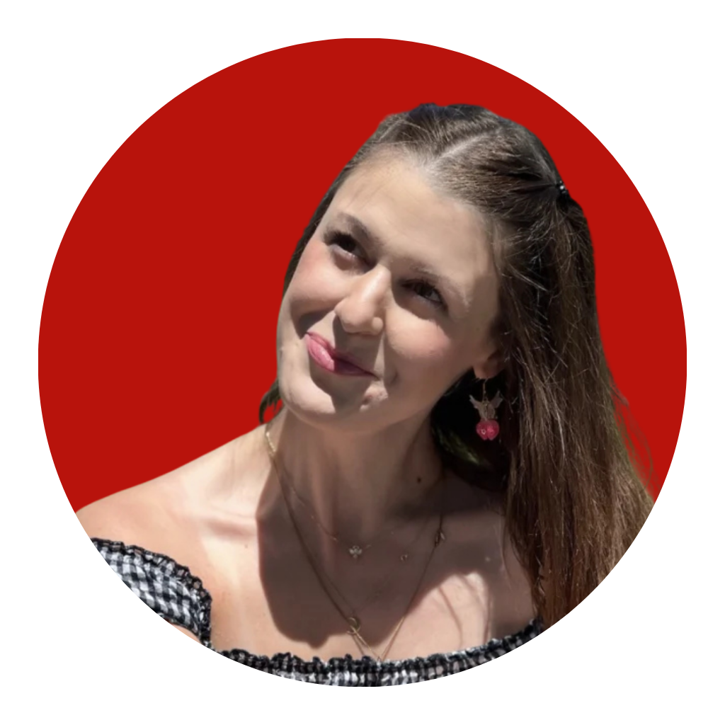 A young woman with long brown hair and cherry earrings looks up coyly against a red background.