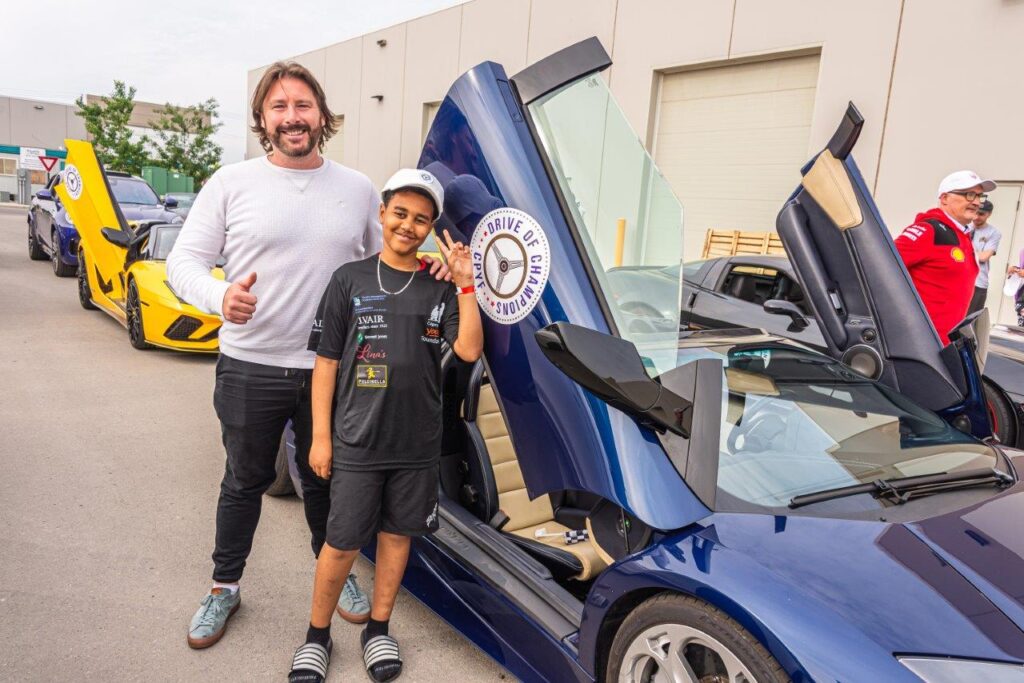 Man and boy pose with a blue supercar with butterfly doors open at Drive of Champions event.