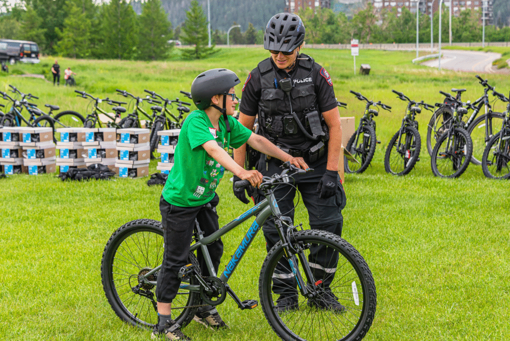 Police officer helps child with bicycle at community event with many bikes.