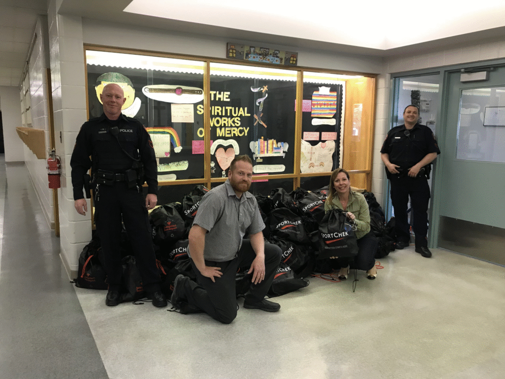 Police officers and a woman with Sport Chek bags in a school hallway