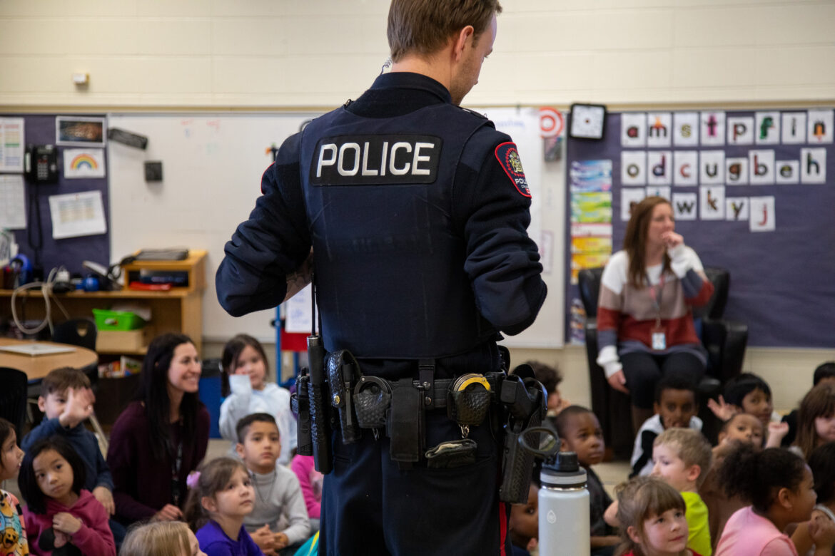 Police officer presents to engaged elementary school children in a classroom.