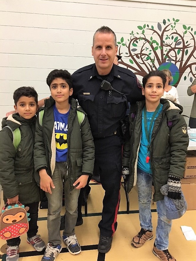 Police officer with three young boys, one holding a hedgehog lunchbox.