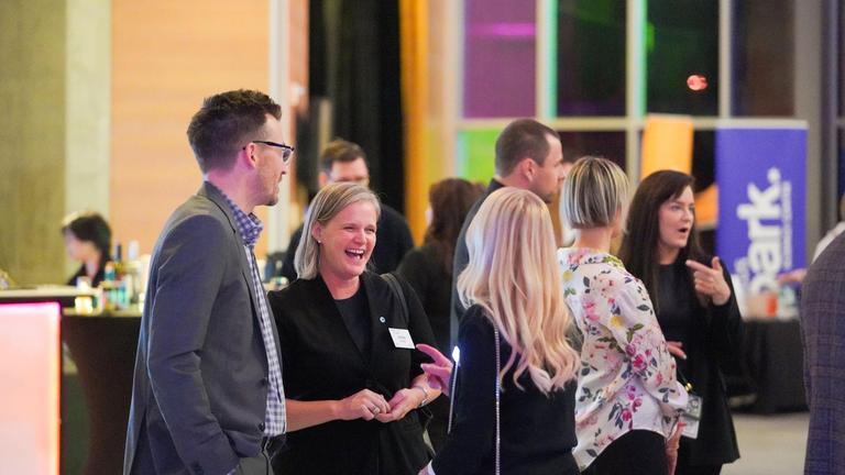 Group of professionals networking at an event, with focus on a laughing woman in a black blazer.
