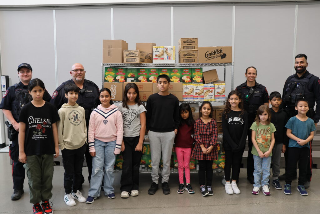 Police officers and children stand beside donation shelves stocked with food