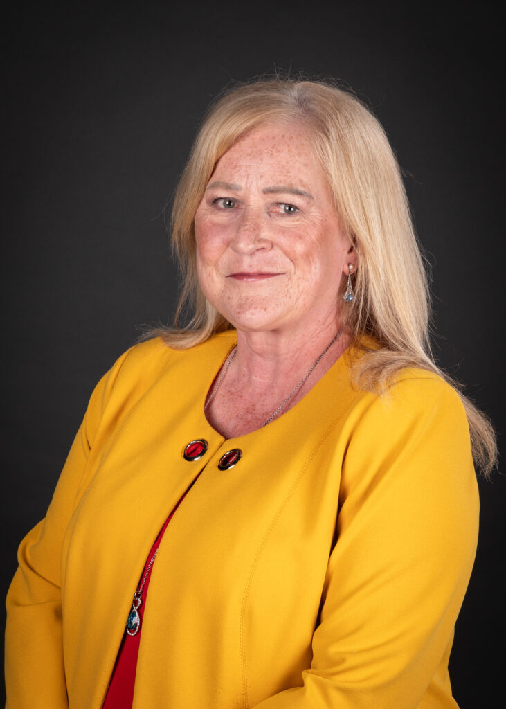 Woman with blonde hair wearing a yellow jacket and red dress