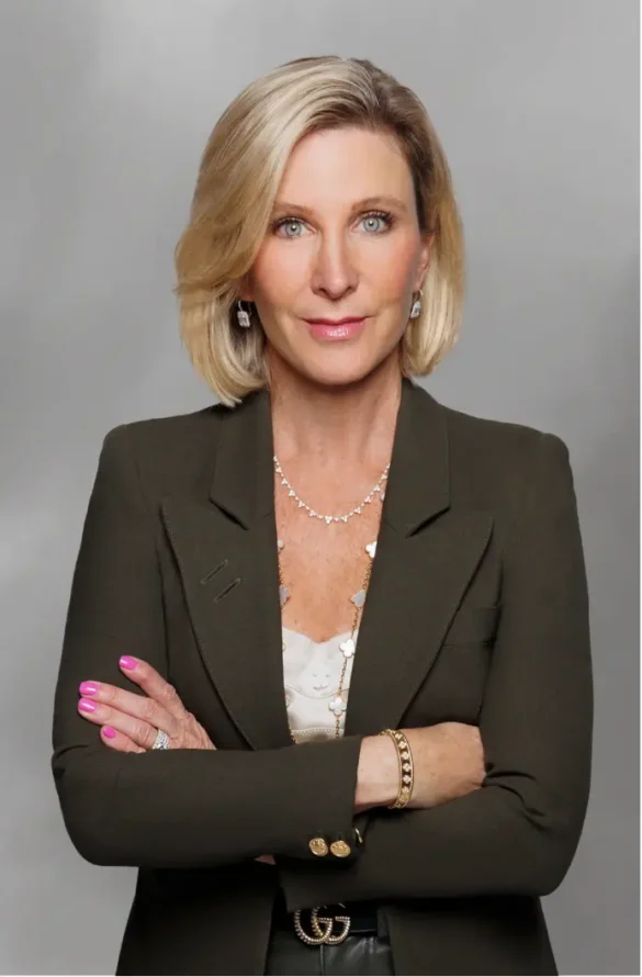 Blonde woman in a green blazer with arms crossed, diamond necklace, and a GG belt.