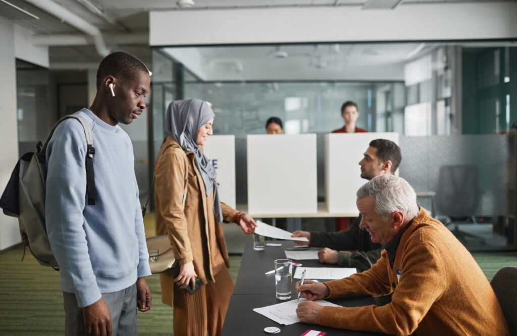 A diverse group of adults engaged in voting at an indoor polling station.