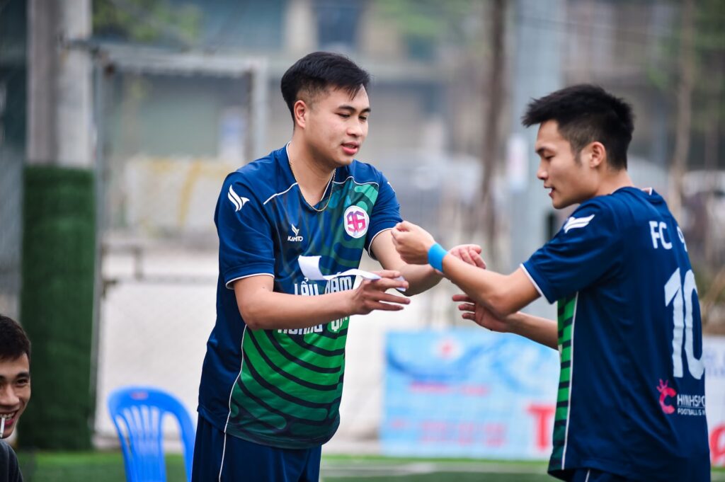 Two football players on an artificial turf field in Hanoi, Vietnam, preparing for a game.