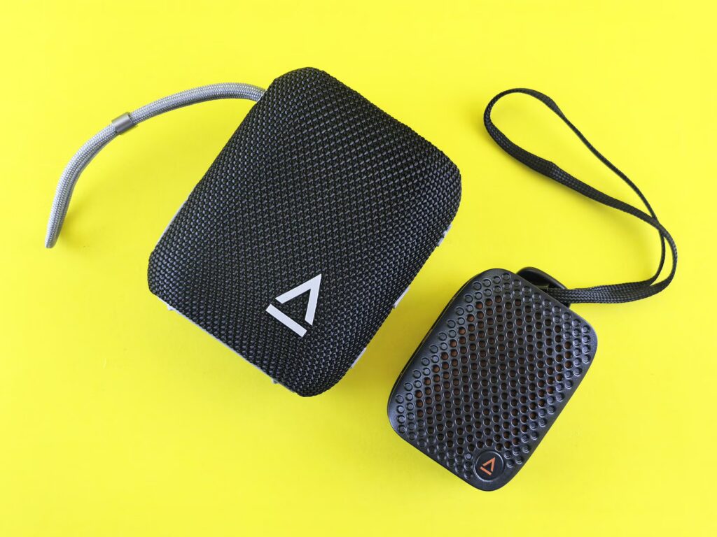 Two portable black speakers with textured surfaces on a bright yellow background, perfect for tech designs.
