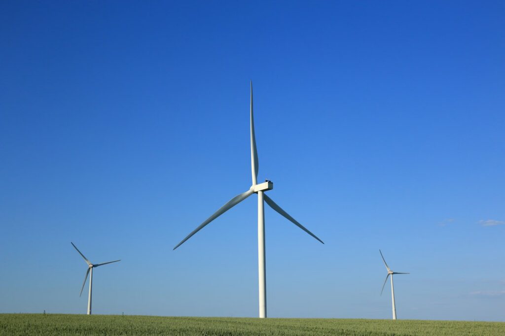 Three wind turbines in a rural field under a bright blue sky, symbolizing renewable energy and sustainability.