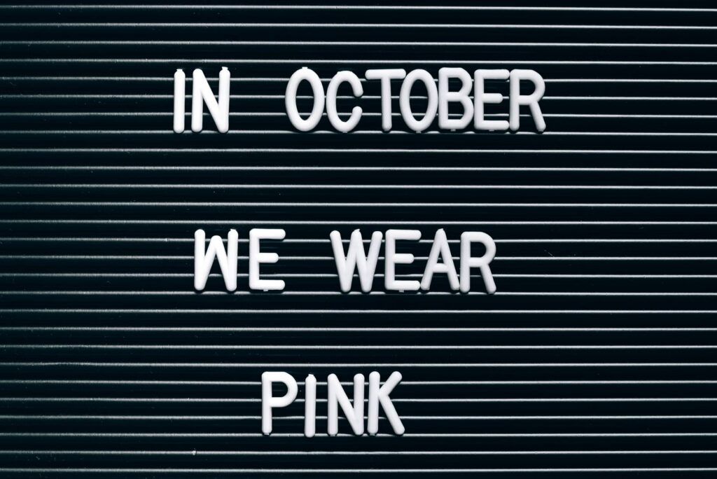Minimalist sign highlighting breast cancer awareness in October with 'In October We Wear Pink'.