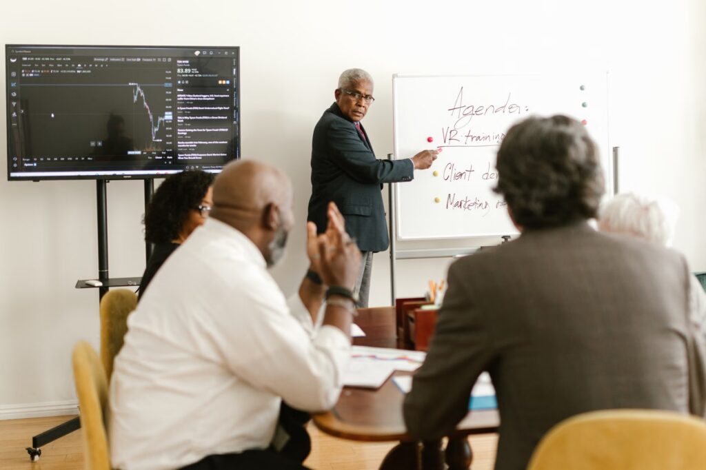 A diverse group of professionals having a meeting in an office setting, discussing on a whiteboard.